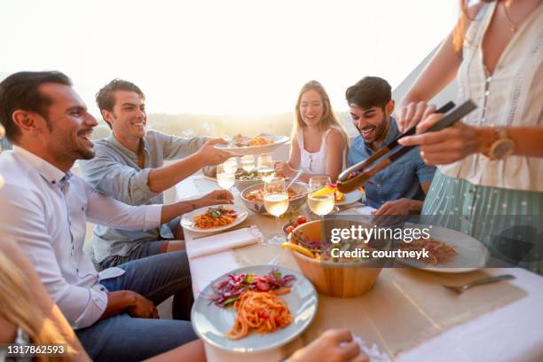 amici e familiari servire insalata su un tavolo al tramonto. - rooftop dining foto e immagini stock