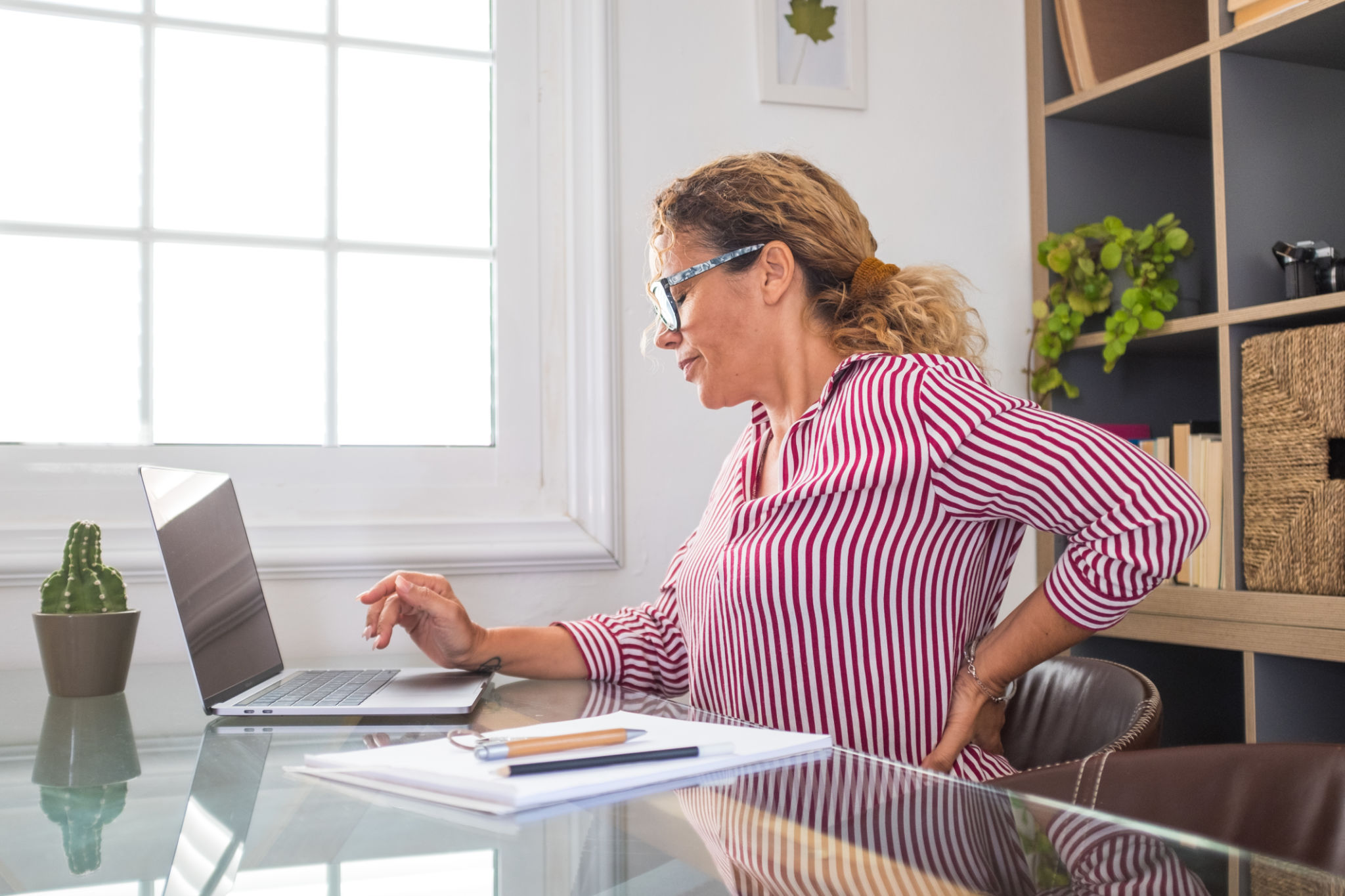 Close up rear view stressed young woman touching lower back feeling discomfort, suffering from sudden pain due to sedentary lifestyle or long computer overwork in incorrect posture at home office. Close up rear view stressed young woman touching lower back feeling discomfort, suffering from sudden pain due to sedentary lifestyle or long computer overwork in incorrect posture at home office.