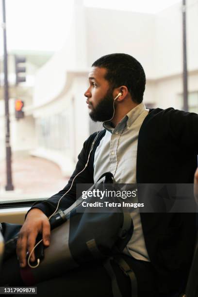 young man traveling on light train wearing earphones - métro léger photos et images de collection