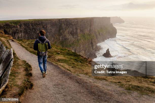 mid adult man walking on the cliffs of moher, the burren, county clare, ireland - ireland travel stock pictures, royalty-free photos & images