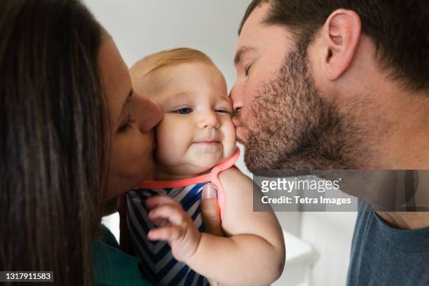 close up of mid adult couple kissing baby daughter on each cheek - mum dad and baby fotografías e imágenes de stock