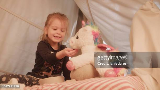 cute, little girl playing with her unicorn toy on cozy, canopy bed - unicorn stock pictures, royalty-free photos & images