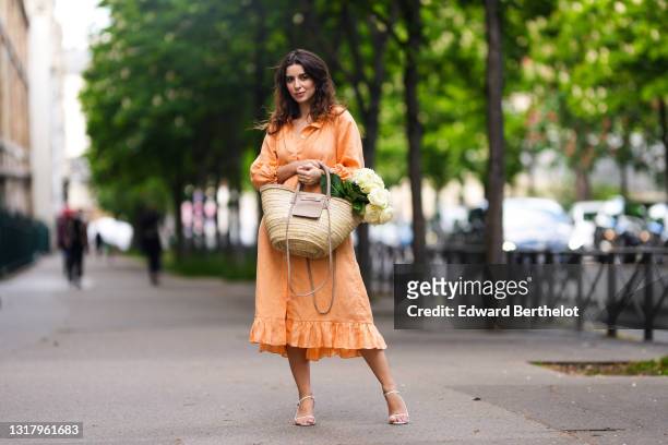 Ketevan Giorgadze @katie.one wears gold earrings, a long buttoned coral loungewear linen The Sleeper dress with puffy sleeves, gold rings, a wicker...