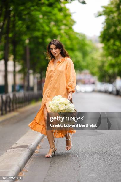 Ketevan Giorgadze @katie.one wears gold earrings, a long buttoned coral loungewear linen The Sleeper dress with puffy sleeves, gold rings, a wicker...