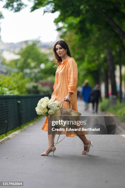Ketevan Giorgadze @katie.one wears gold earrings, a long buttoned coral loungewear linen The Sleeper dress with puffy sleeves, gold rings, a wicker...