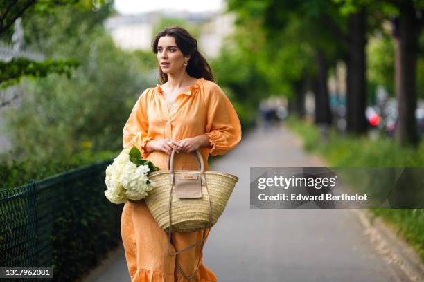 Ketevan Giorgadze @katie.one wears gold earrings, a long buttoned coral loungewear linen The Sleeper dress with puffy sleeves, gold rings, a wicker...