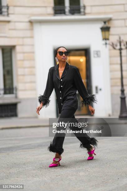 Emilie Joseph @in_fashionwetrust wears silver rhinestones Isabel Marant earrings, black sunglasses, a black ribbed buttoned long shirt with black...