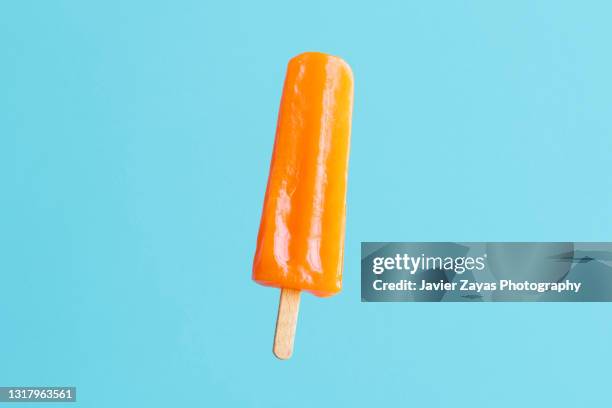 orange flavoured and colored popsicle stick on blue/turquoise background - ice cream imagens e fotografias de stock