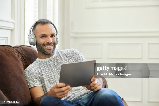 portrait of smiling man holding digital tablet - familie sofa stock pictures, royalty-free photos & images