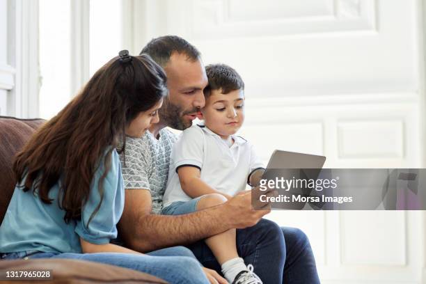 family sharing digital tablet in living room - familie sofa stock pictures, royalty-free photos & images