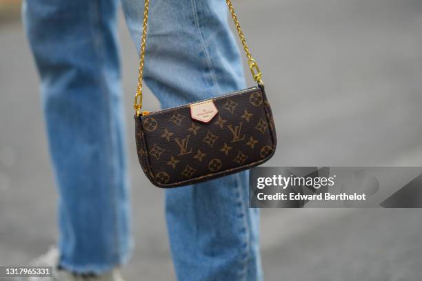 Djebril Irid wears blue faded denim ripped jeans pants with outside pockets, white Triple S Balenciaga sneakers, a brown Louis Vuitton monogram in...