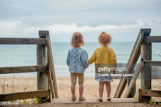 two little girls holding hands and looking out to sea - barefoot girl stock pictures, royalty-free photos & images