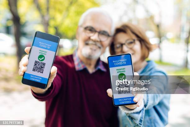 pareja de ancianos mostrando teléfonos inteligentes con certificados electrónicos de vacunación - portraits of people passport fotografías e imágenes de stock