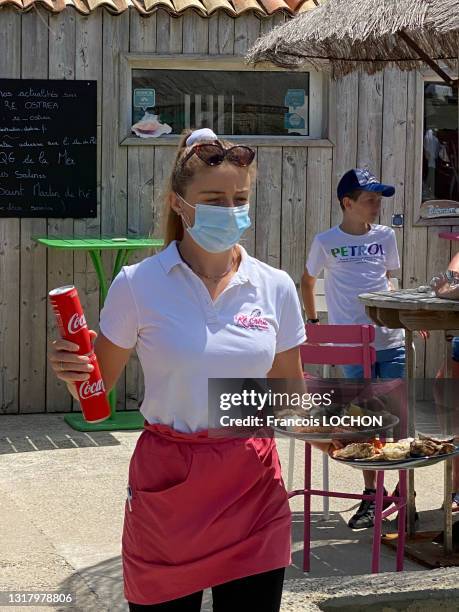 Serveuse avec un masque servant des huitres et des canettes de Coca Cola sur la terrasse de restaurant "Ré Ostrea", 3 juillet 2020,...