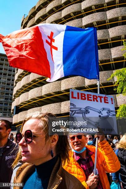 Un militant porte une pancarte "LIBERTÉ! RENDEZ NOUS NOS VIES" et un drapeau français avec la croix de Lorraine lors du rassemblement...