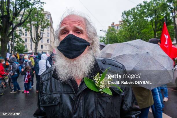 Un homme agée habilillé en noir porte des brins de muguets sur son blouson lors de la manifestation rassemblant 3000 personnes le 1er mai 2021 à Lyon.