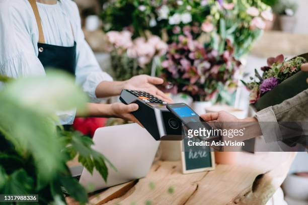 cropped shot of young asian man shopping at the flower shop. he is paying for a bouquet with his smartphone, scan and pay a bill on a card machine making a quick and easy contactless payment. nfc technology, tap and go concept - new normal concept stock pictures, royalty-free photos & images