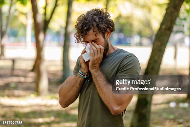 man with seasonal flu is walking in park and coughing in paper tissues. - blowing nose stock pictures, royalty-free photos & images