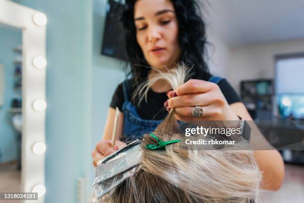 stylish hairdresser holding a lock of hair of female hairstyle while highlights hair - mèche foto e immagini stock