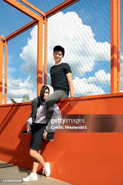 girl carrying boyfriend's legs on shoulder sitting on fenced railing - sitting on wall stock-fotos und bilder