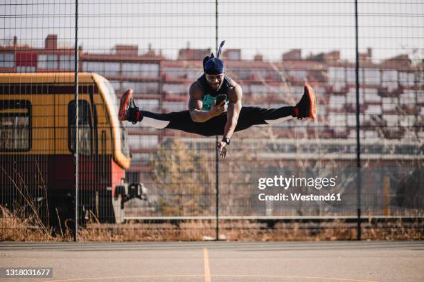 african man using mobile phone while jumping on sports court - legs apart imagens e fotografias de stock