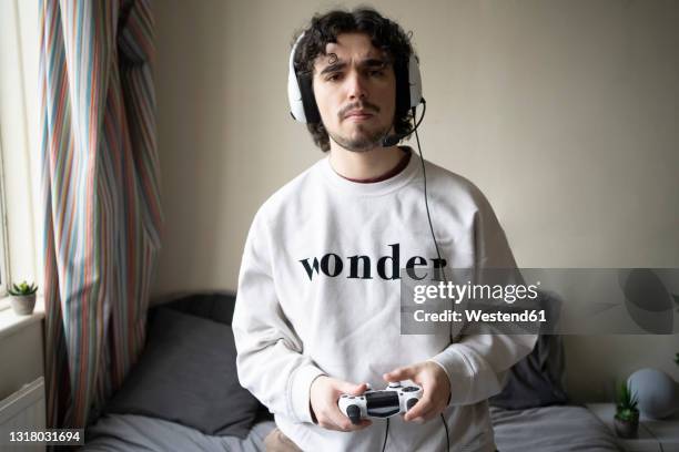 man with headset holding game controller at home - mann headset stock-fotos und bilder