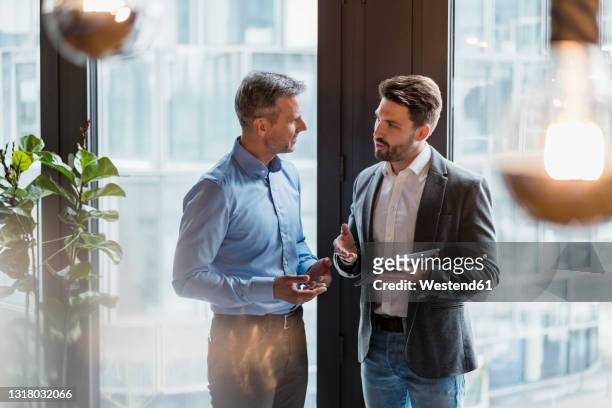 male professionals discussing over digital tablet in office - two people talking office stock pictures, royalty-free photos & images