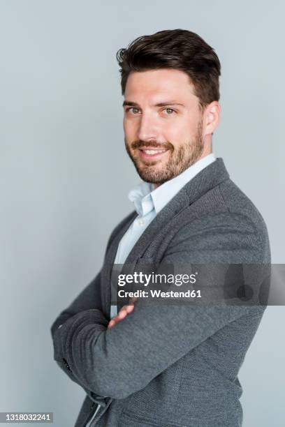 smiling male professional with arms crossed standing by gray background - gray jacket ストックフォトと画像