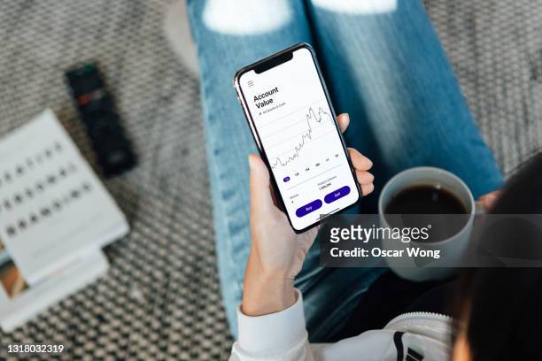 woman using stock trading app on mobile phone at home - handelsfinanzierung stock-fotos und bilder