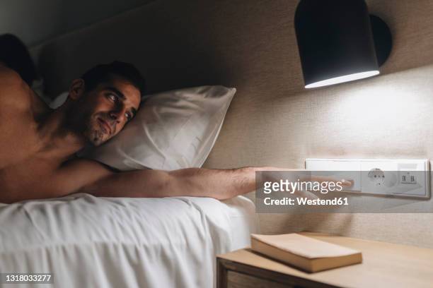 mid adult man turning off light while lying on bed - turning on light switch stock pictures, royalty-free photos & images