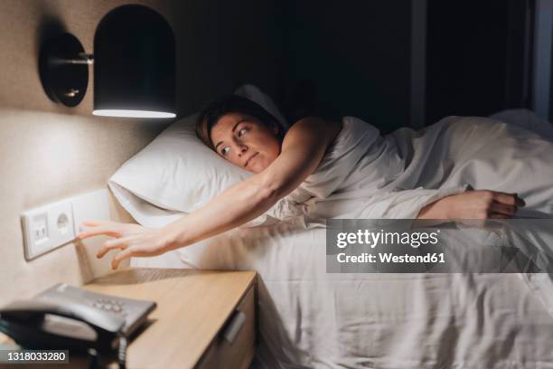 mid adult woman turning off light while lying on bed - turning on light switch stock pictures, royalty-free photos & images