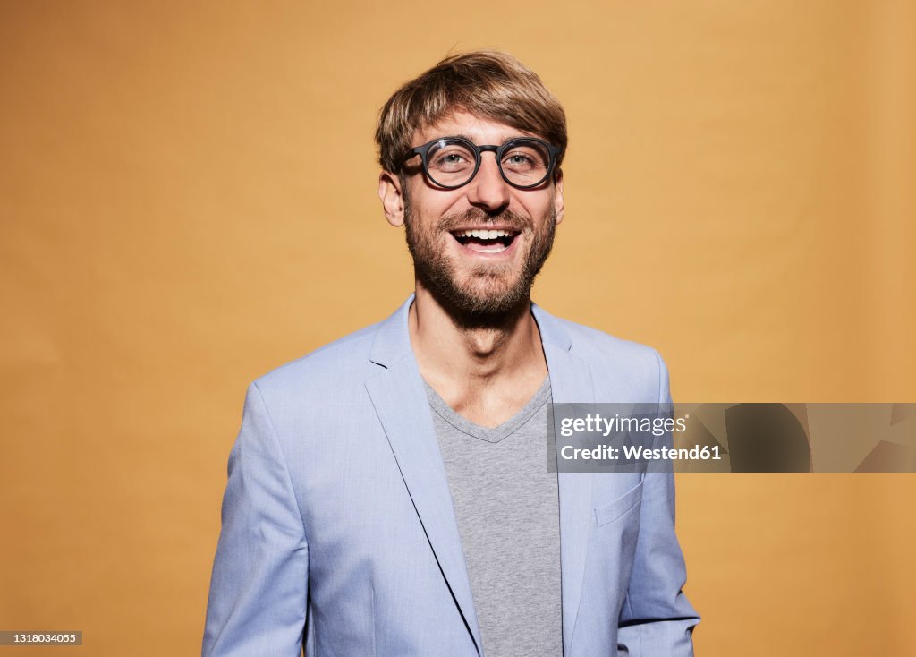 Man wearing eyeglasses laughing in front of yellow wall