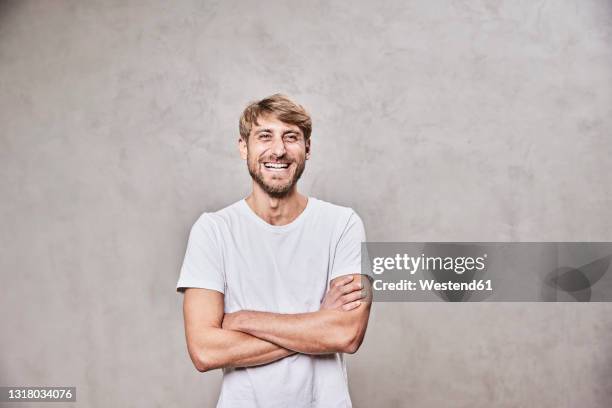 happy man with arms crossed standing in front of wall - arms folded imagens e fotografias de stock