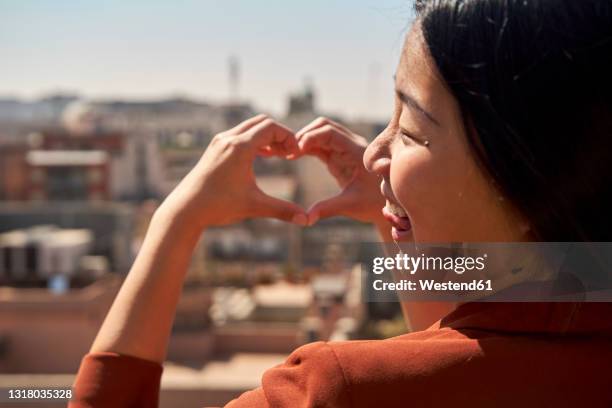 smiling woman gesturing heart shape on sunny day - barcelona hotel stockfoto's en -beelden