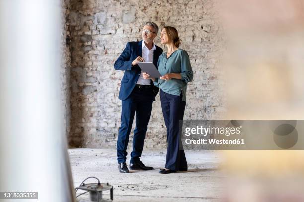 male and female architects discussing while standing at construction site - homme ipad photos et images de collection