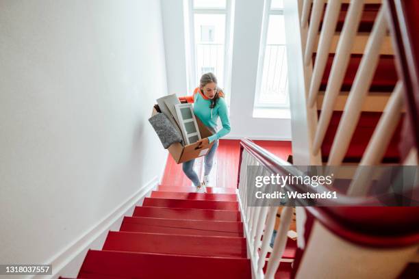 young woman carrying cardboard boxes while moving up on staircase at home - woman on the move stock pictures, royalty-free photos & images