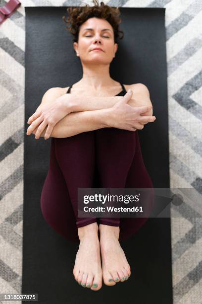 woman lying on exercise mat in fetal position at home - hugging knees bildbanksfoton och bilder