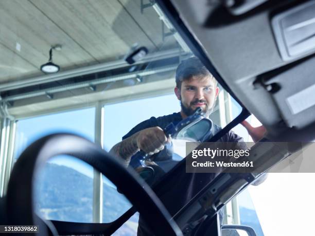 repairman cleaning windshield of car at garage - windschutzscheibe stock-fotos und bilder