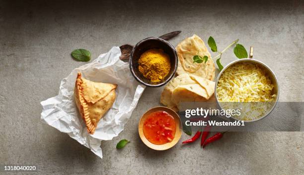studio shot of samosa dumpling on paper napkin, bowl of basmati rice, chili dipping sauce, naan bread and red chili peppers - garam masala stock pictures, royalty-free photos & images