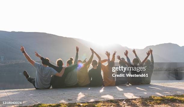 cheerful male and female friends sitting together on promenade during sunny day - unity foto e immagini stock