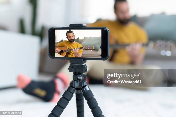 handsome man filming while playing guitar at home - tripod stock-fotos und bilder