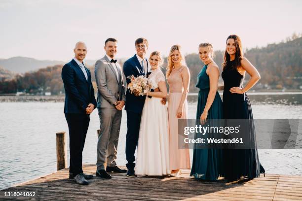 bride and groom standing along with friends on jetty over lake - wedding guest stock-fotos und bilder