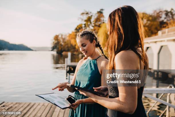 female planners discussing over clipboard near lake - wedding planner stock-fotos und bilder