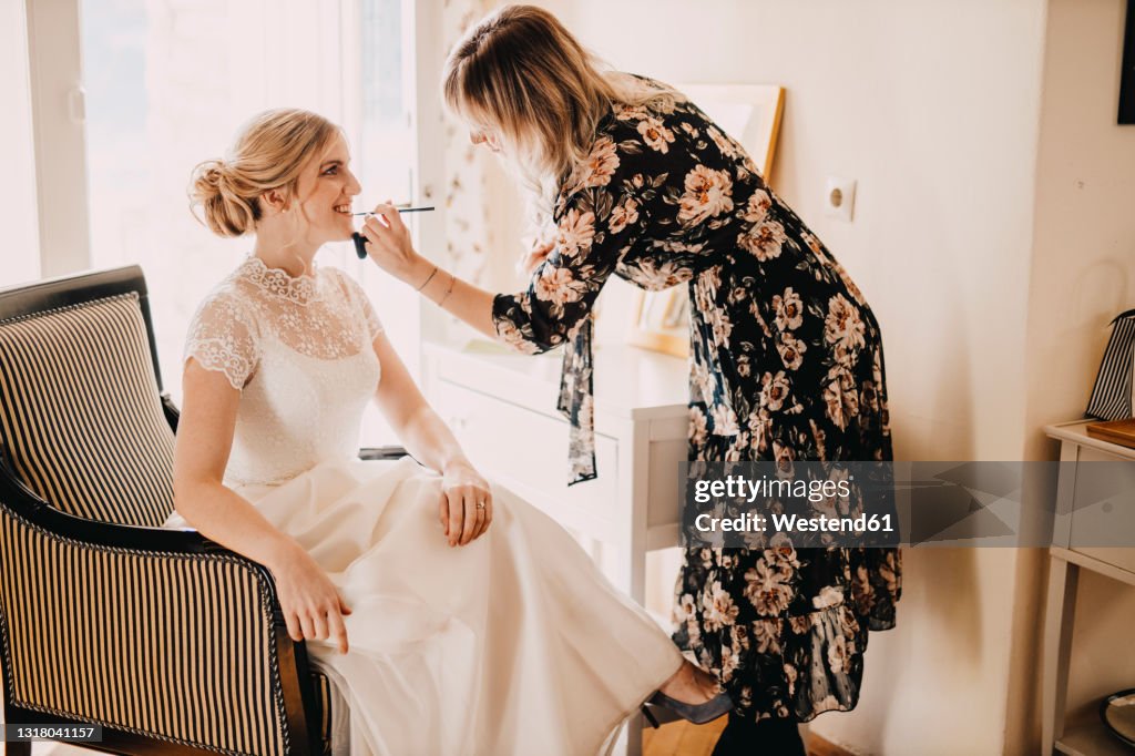 Make-up artist applying lipstick on excited bride during wedding
