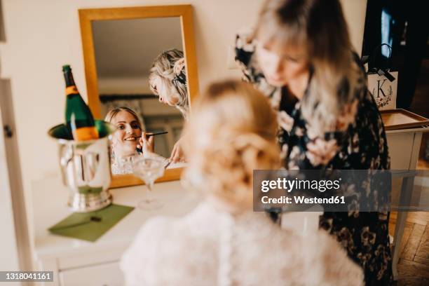 bride looking in mirror while beautician applying make-up during wedding - wedding planner stock-fotos und bilder