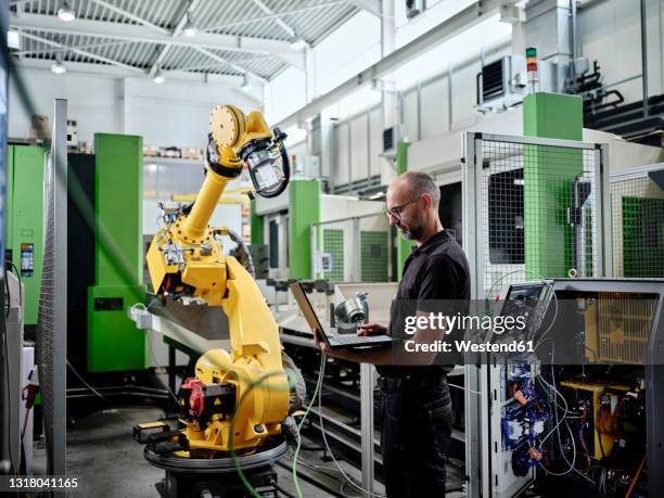 male engineer using laptop by robotic arm - mechatronics fotografías e imágenes de stock