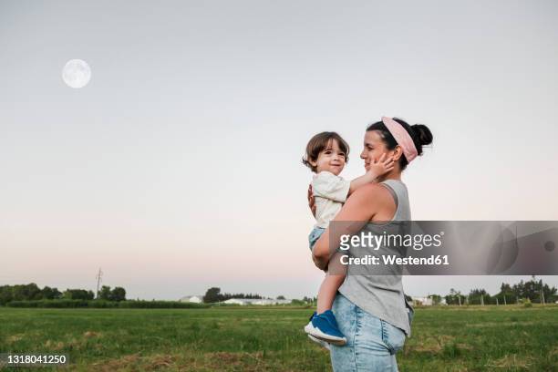 mother looking while carrying son during sunset - baby standing stock pictures, royalty-free photos & images
