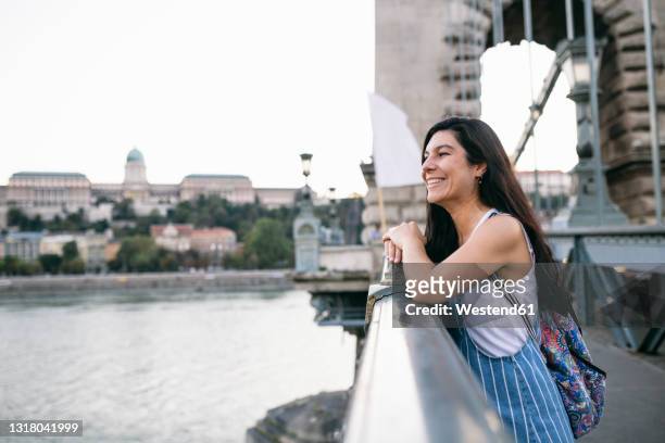 smiling woman looking away while leaning on bridge railing - railing stockfoto's en -beelden