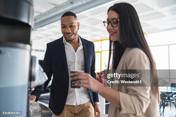 smiling businesswoman taking coffee by male colleague at office - kaffeemaschine stock-fotos und bilder