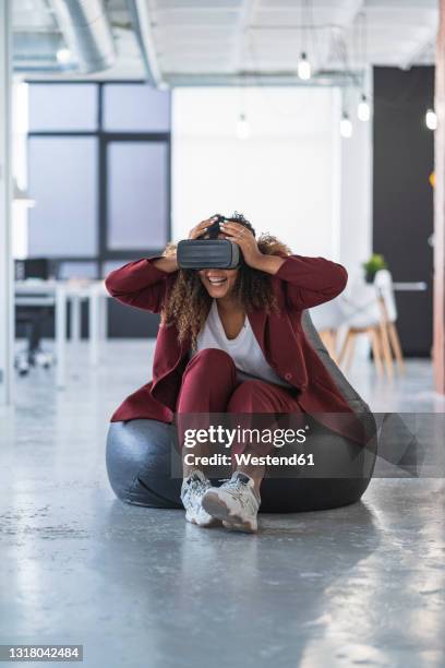 happy businesswoman watching virtual reality through headset at office - beanbag photos et images de collection